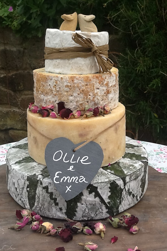 The Cornish Yarg Delight features 4 tiers including, Cornish Yarg, Stilton, Camembert and Chedder. This cake is decorated with rose buds, a grey slate with the names "Ollie & Emma" on, two decorative mice on the top. and ivory raffia around the top tier.