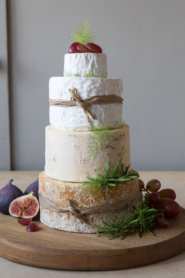 Cheddar & Stilton Celebration cheese cake decorated with raffia, shown with figs and grapes on wooden board
